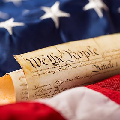 The U.S. Constitution's "We the People" on parchment against the United States flag.